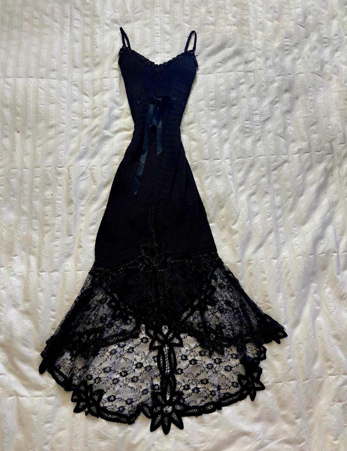 Black spaghetti strap prom dress with a lace flared hem laid on a white quilted bedspread.