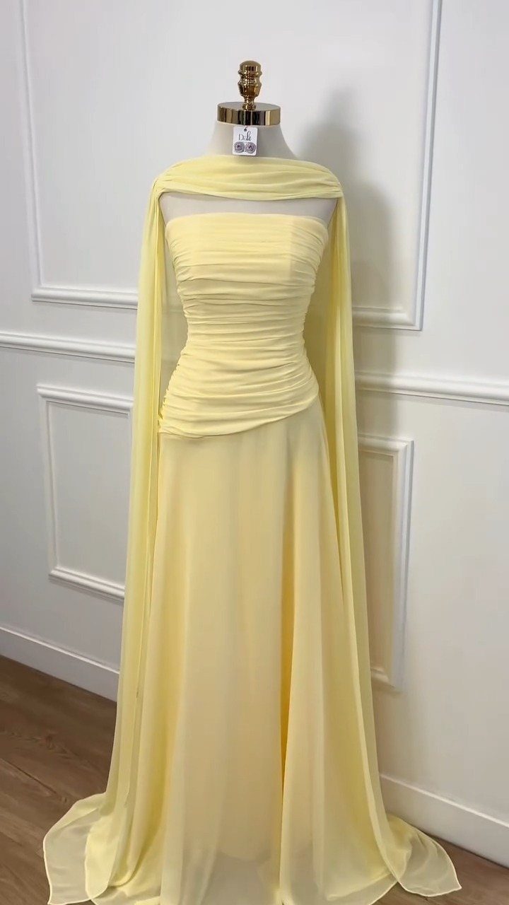 A pale yellow strapless ruched chiffon prom dress with a matching capelet on a mannequin.