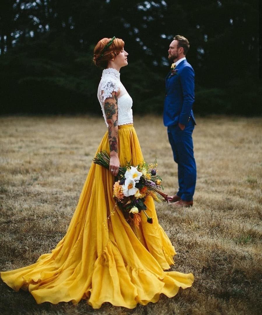 Woman in a white lace top and voluminous yellow skirt holding a bouquet in a field.