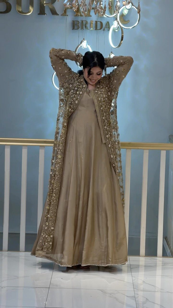Woman in a champagne gown and gold embroidered lace duster coat standing indoors.