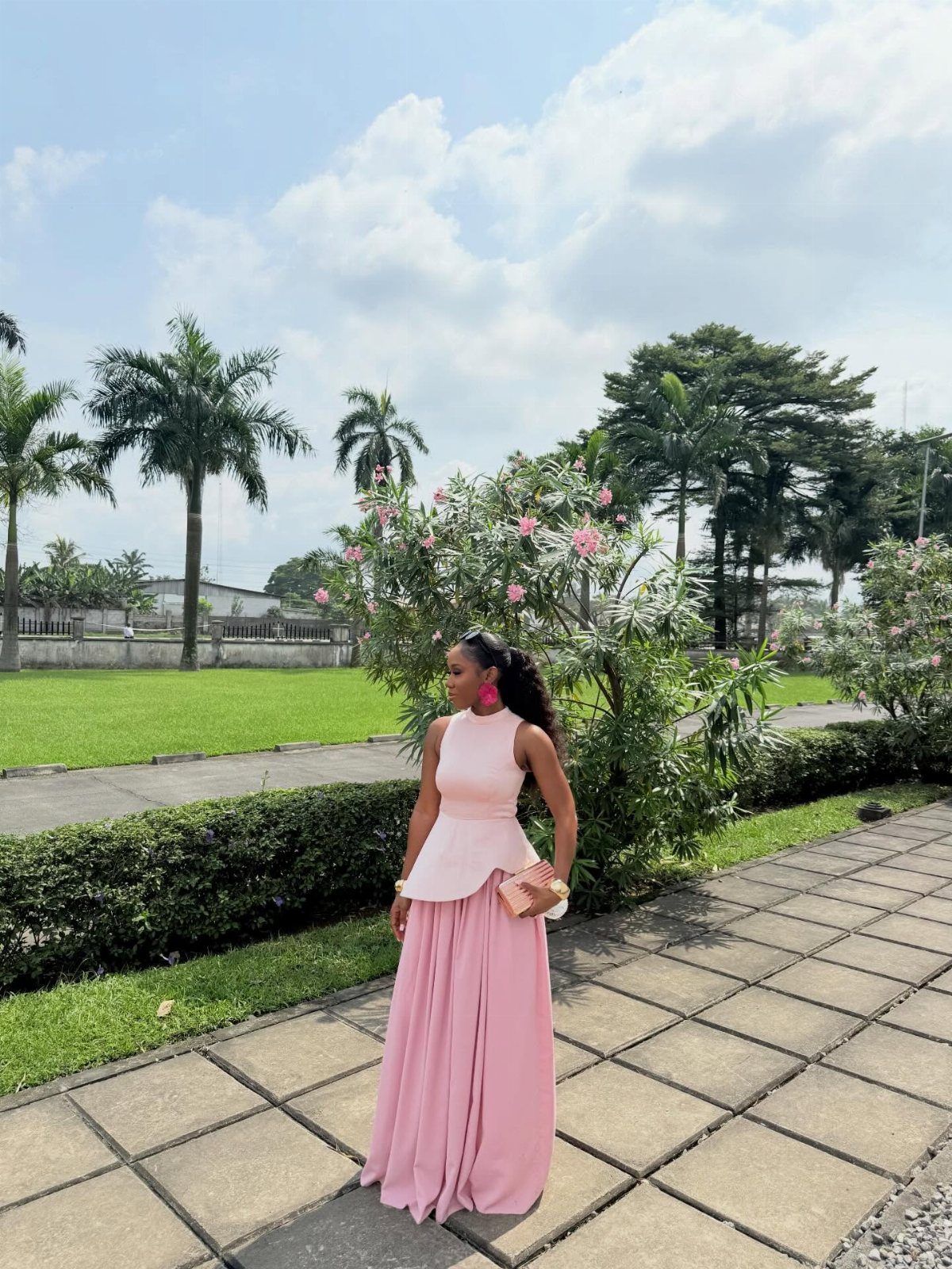 Woman in a pink sleeveless maxi dress standing on a stone path in a park.
