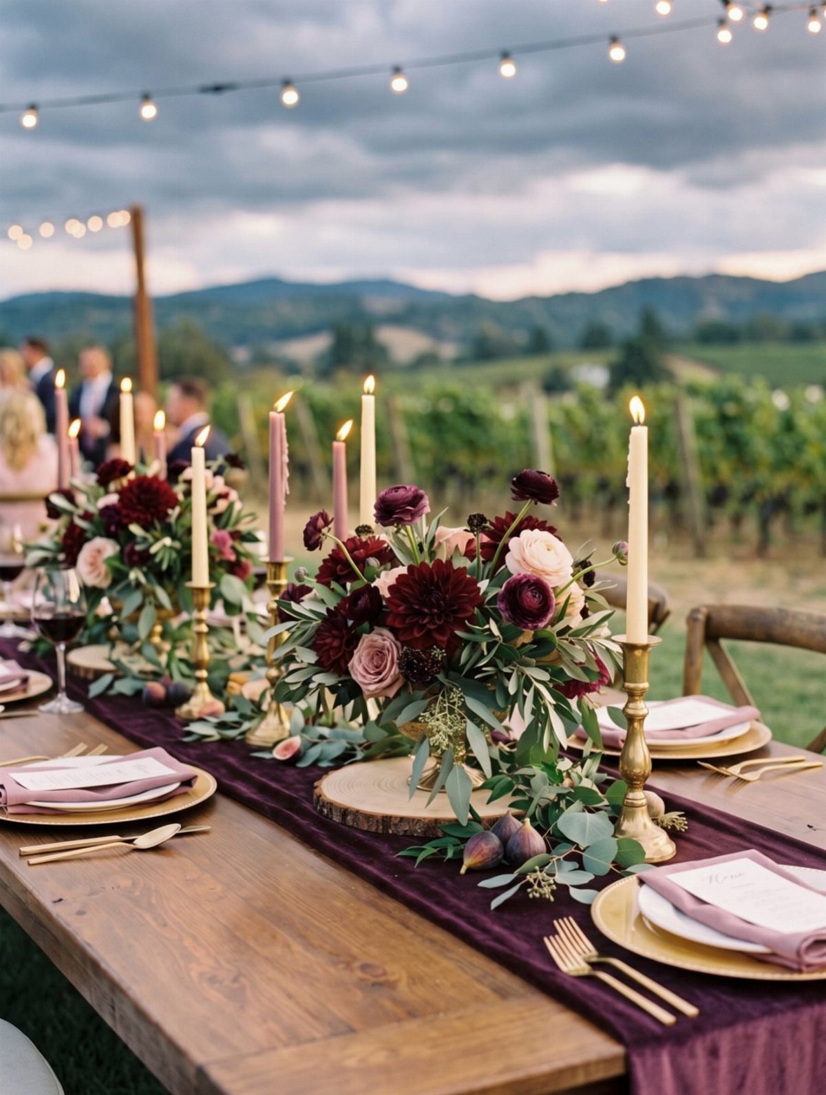 Burgundy and pink floral centerpieces with taper candles on a long wooden wedding reception table.
