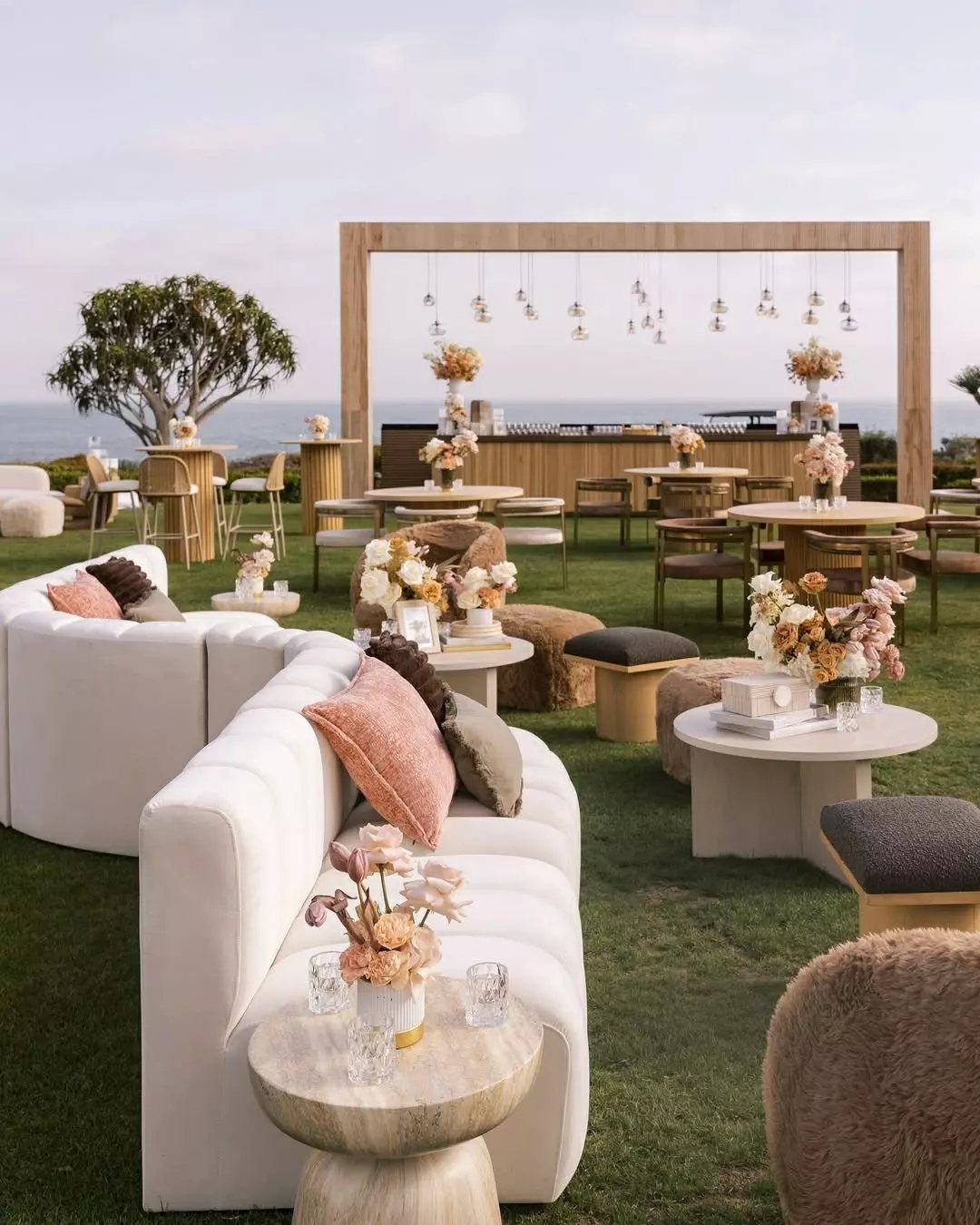 White curved sofas and small tables with floral arrangements arranged on a green lawn outdoors.