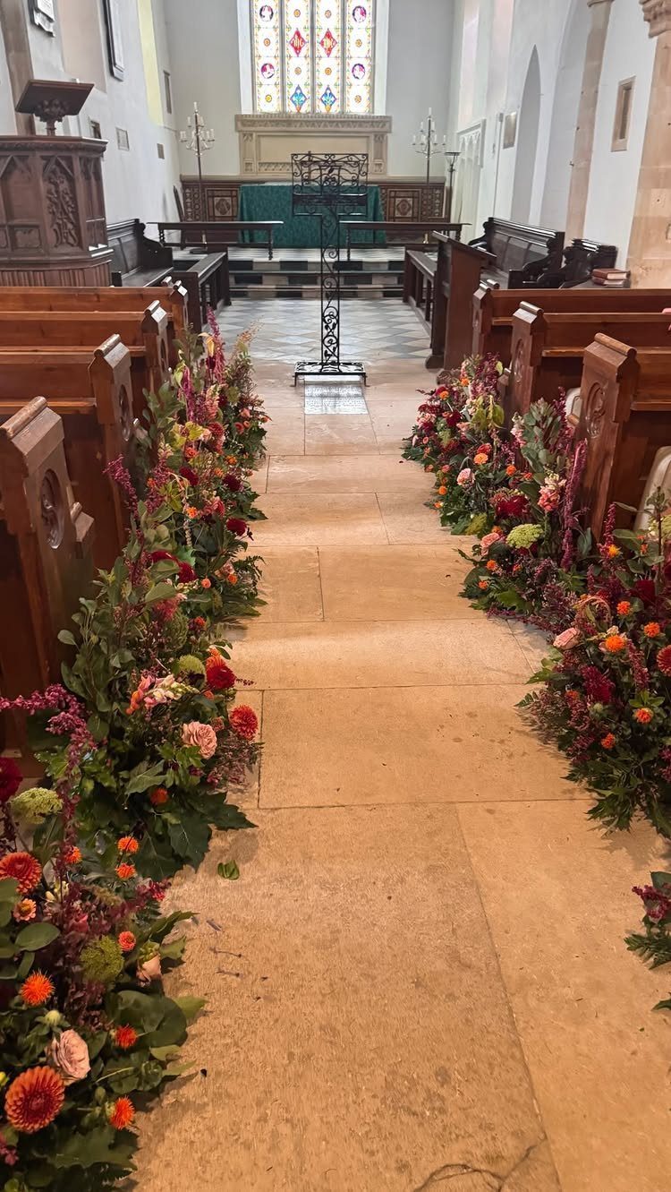 Colorful floral arrangements lining the wooden pews of a church aisle leading to the altar.
