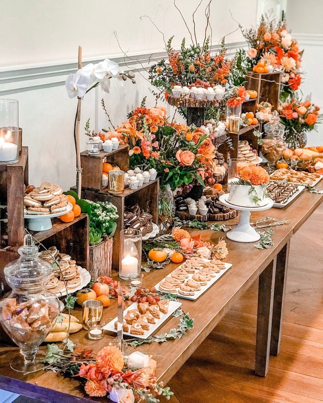 A long wooden table filled with various autumn-themed cookies, pastries, and floral centerpieces.