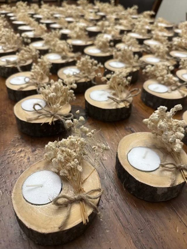 Small wooden log slices with tea light candles and dried flowers on a wooden table.