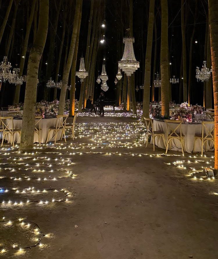 Wedding reception tables and glowing tea lights scattered on the ground in a dark forest.