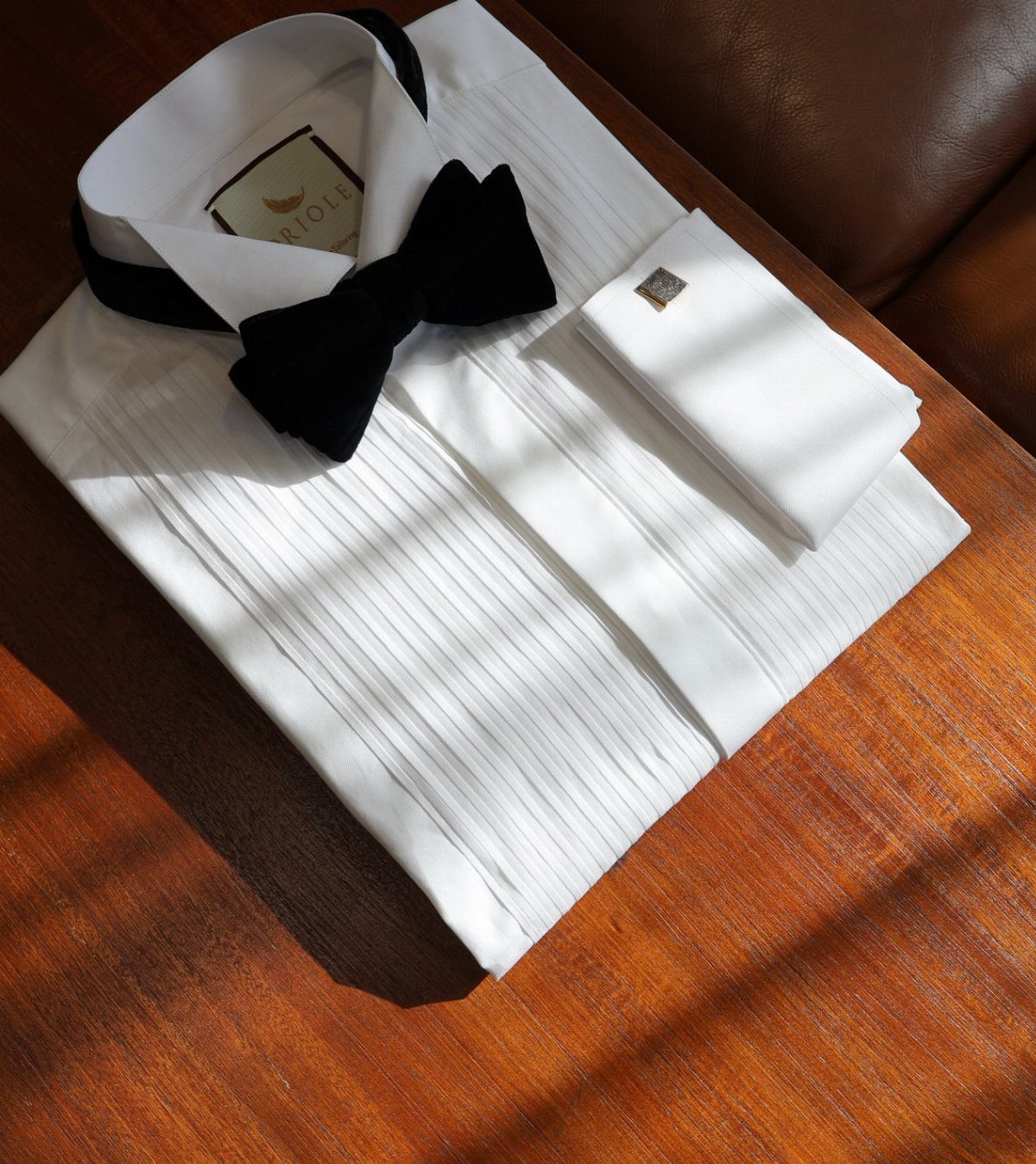 A white pleated tuxedo shirt with a black bow tie and cufflinks on wood.