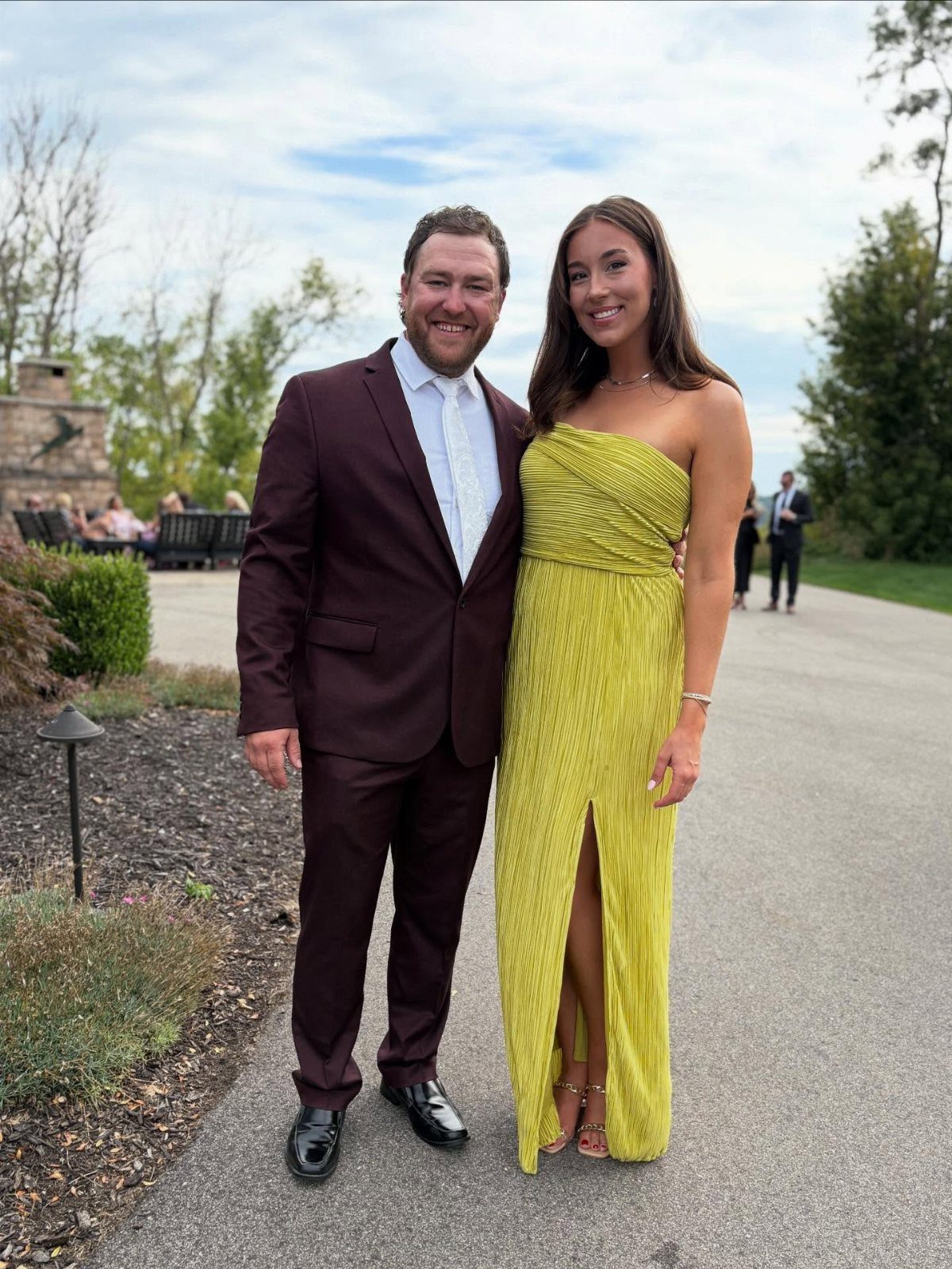A man in a burgundy suit and a woman in a lime green gown posing outdoors.