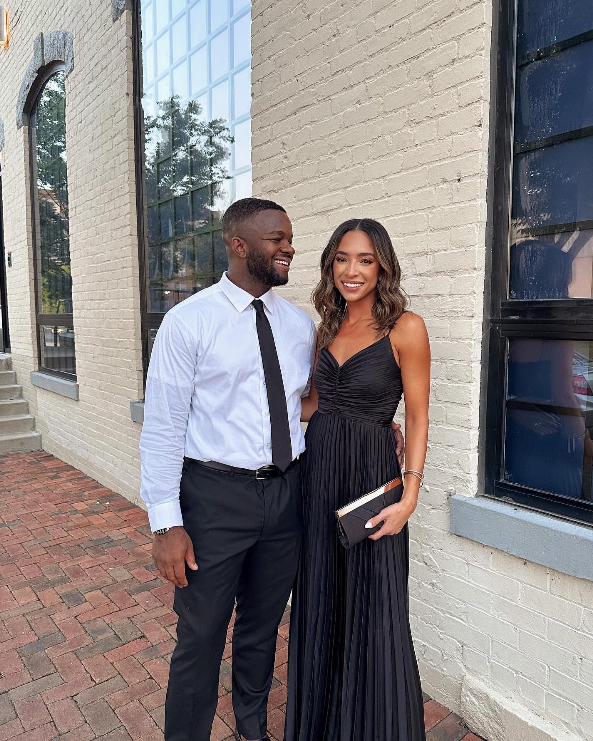 A man in formal attire and a woman in a long black pleated gown posing together.