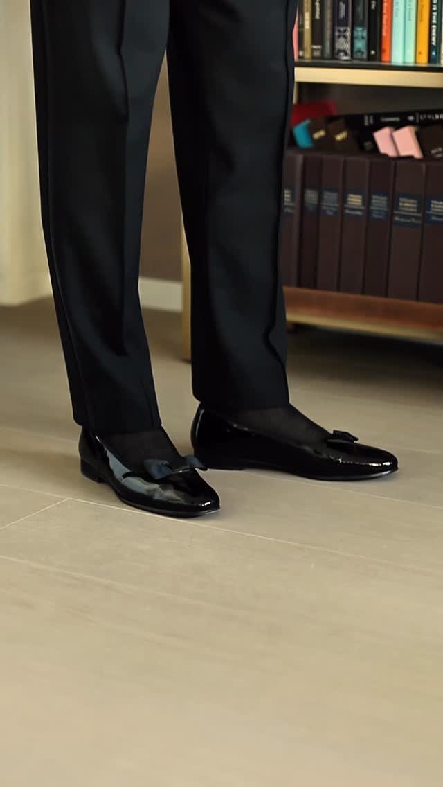 Black patent leather ballet flats with a bow worn with black formal trousers.
