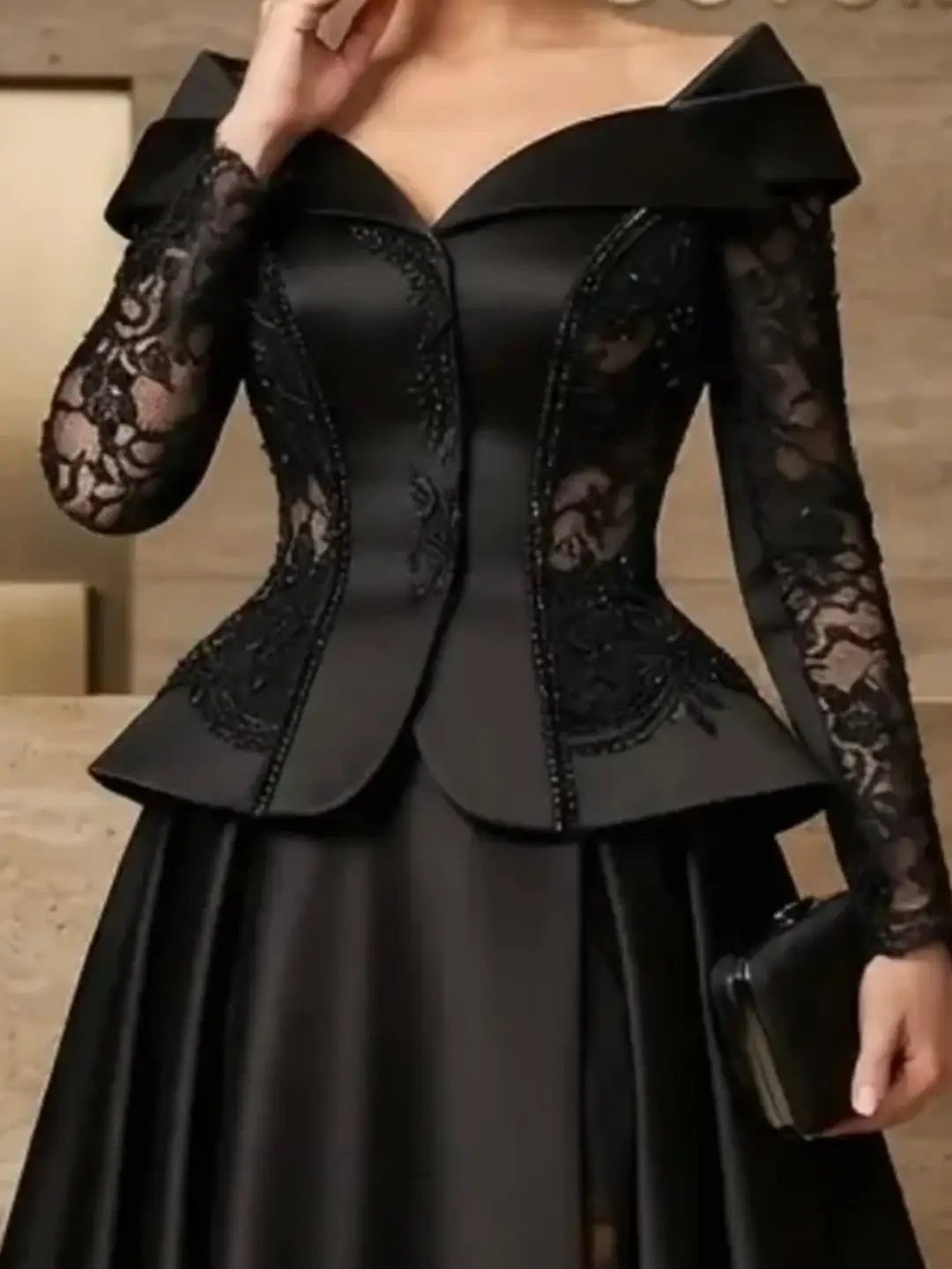 A woman wearing a black formal gown with a structured lace bodice and long sleeves.