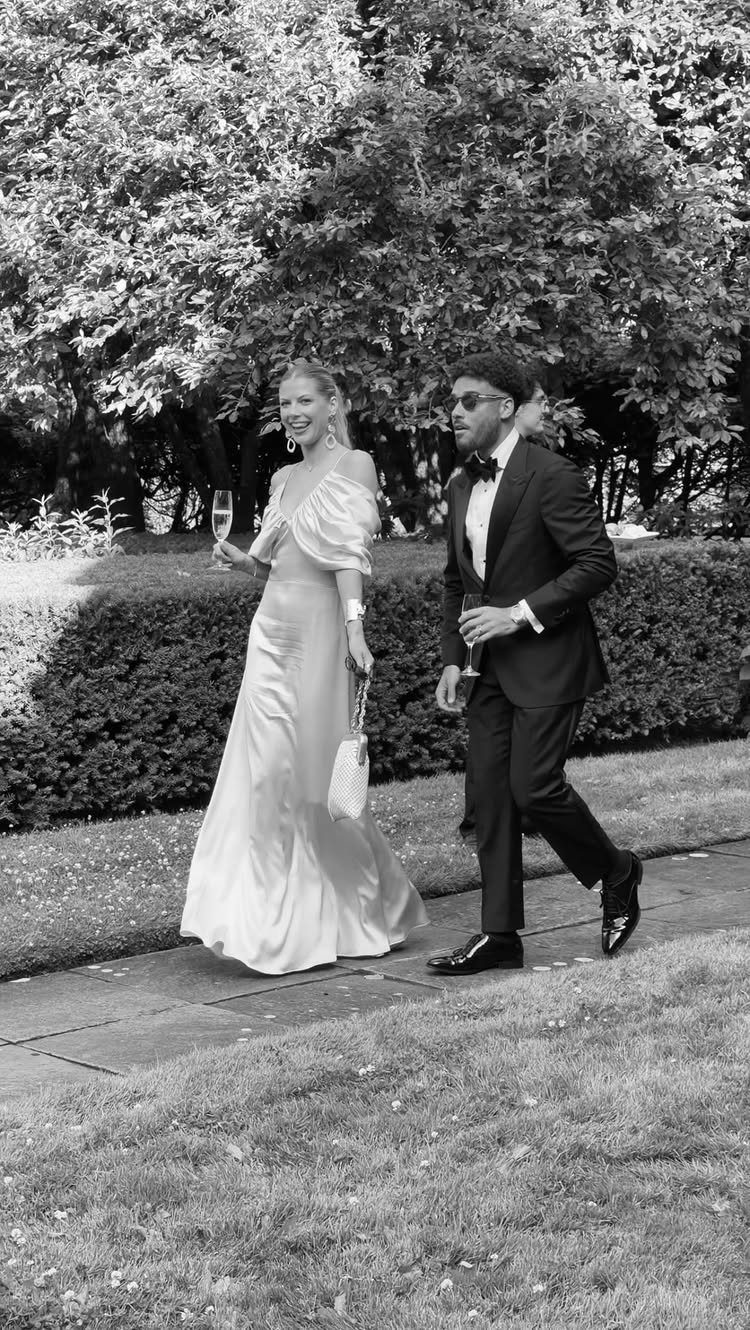 A man in a tuxedo and a woman in an evening gown walking outdoors together.