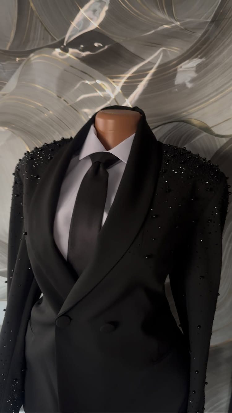 A black beaded tuxedo jacket with a white shirt and black tie on a mannequin.