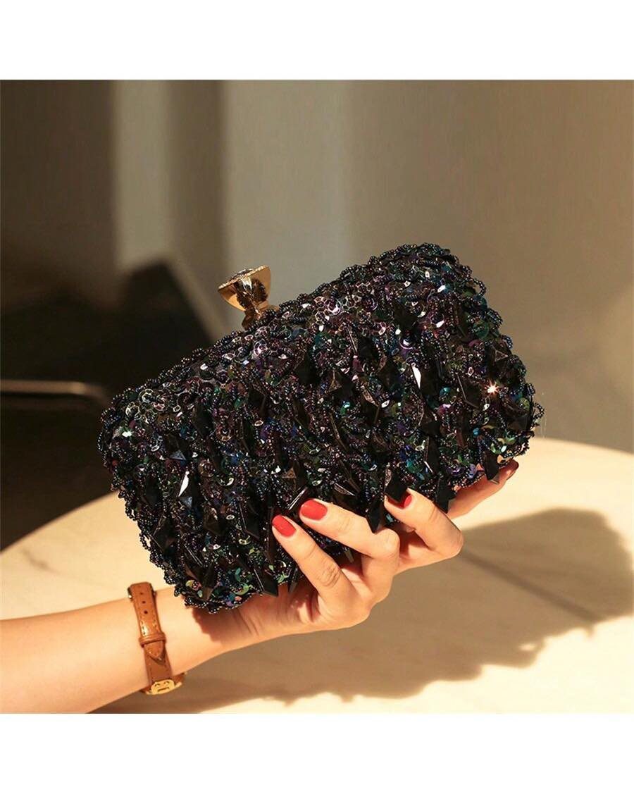 A hand with red nails holding a sparkling black crystal-encrusted clutch bag.