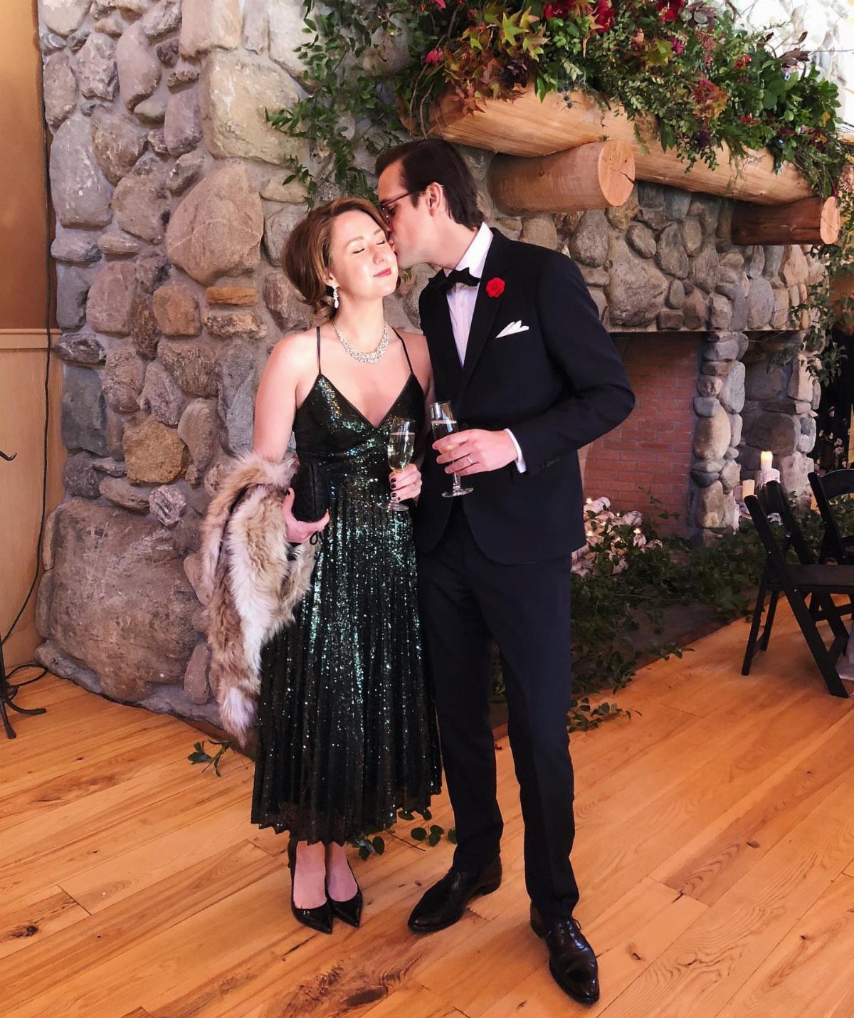 A man in a tuxedo kisses a woman wearing a sparkling green sequined dress.