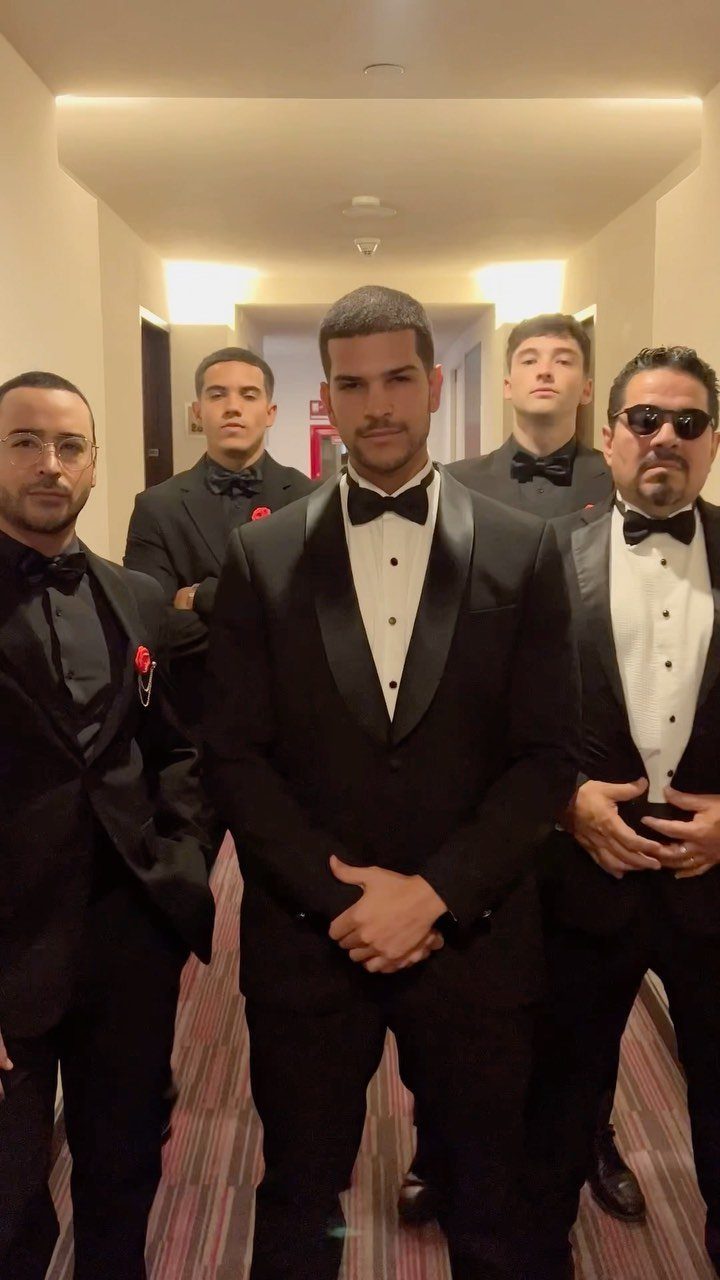 Five men posing in a hallway wearing formal black tuxedos and bow ties.