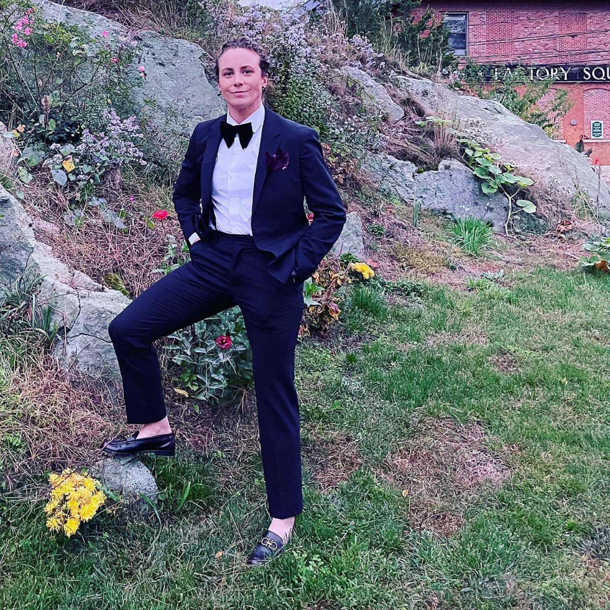 Woman wearing a navy blue suit with a white shirt and black bowtie standing on grass.