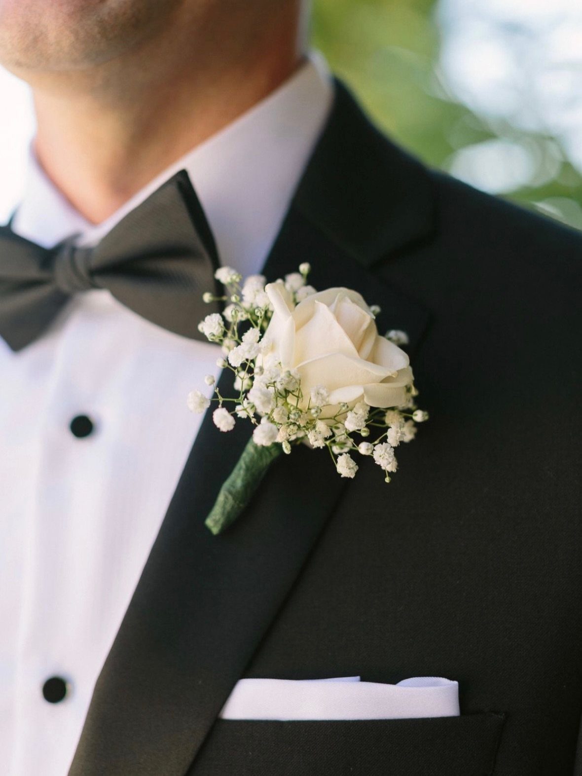 White rose boutonniere with baby's breath on a black tuxedo lapel.