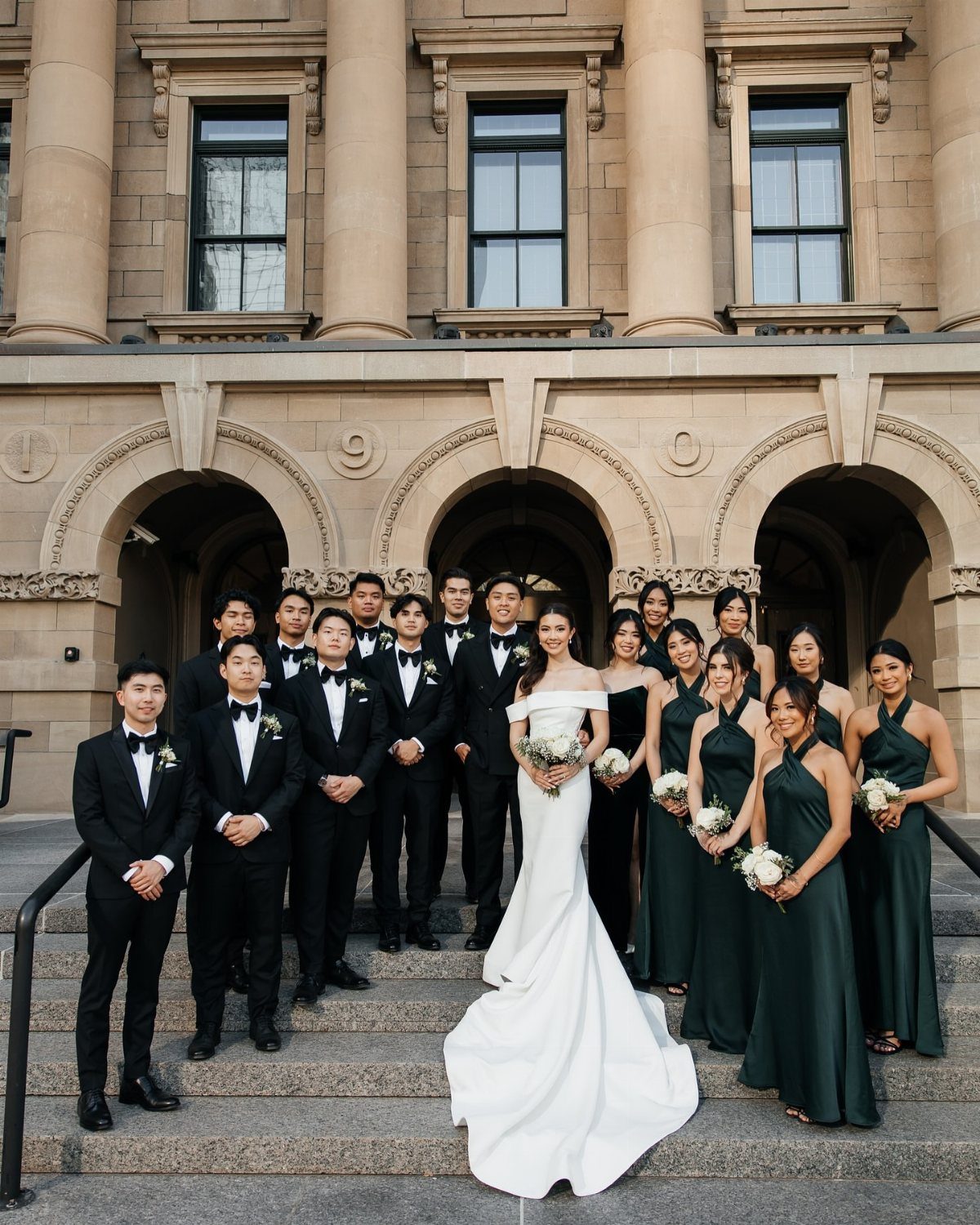 A bride and her bridal party pose symmetrically on the steps of a grand building.