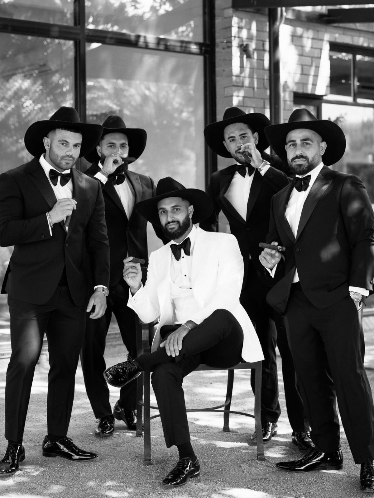 Five men in tuxedos and cowboy hats posing for a group portrait outdoors.