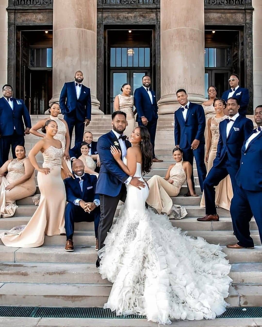A wedding party in navy and champagne attire posing on grand stone steps.