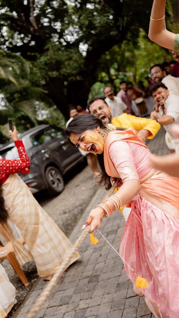 A woman in a pink sari pulls a rope during a competitive tug-of-war game outdoors.