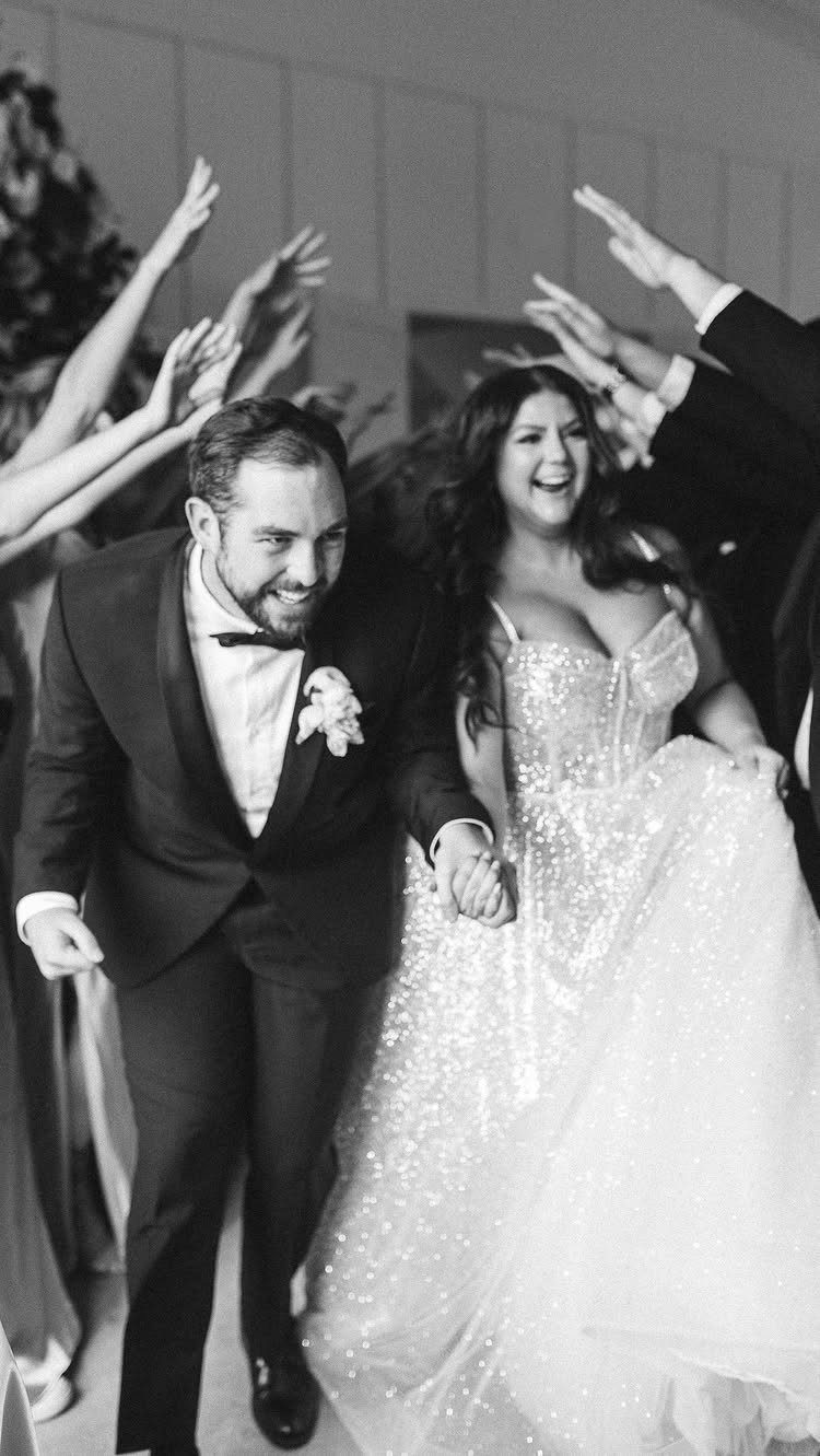 A bride and groom running joyfully through a tunnel of raised hands.