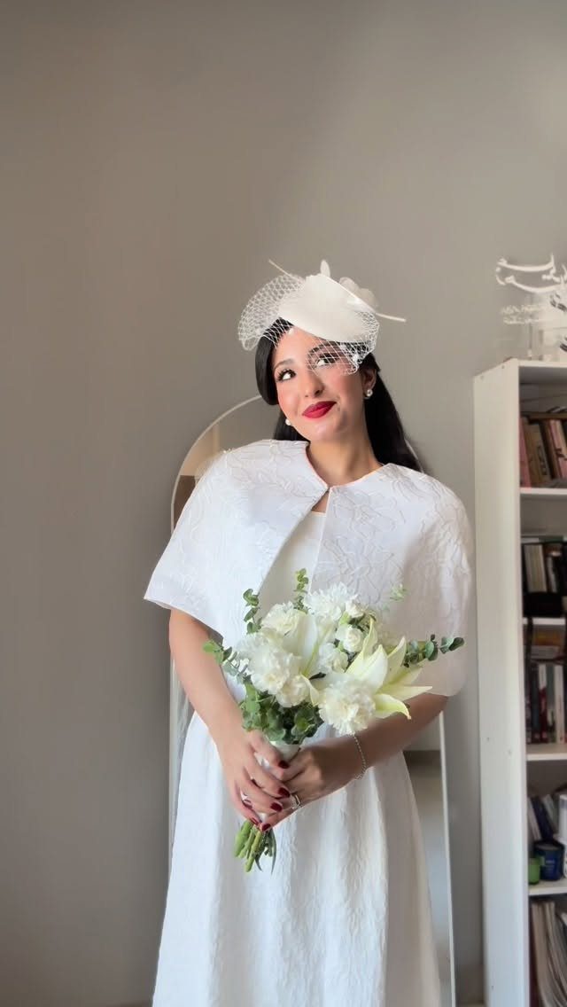 Woman in a white wedding dress and capelet holding a white lily bouquet.