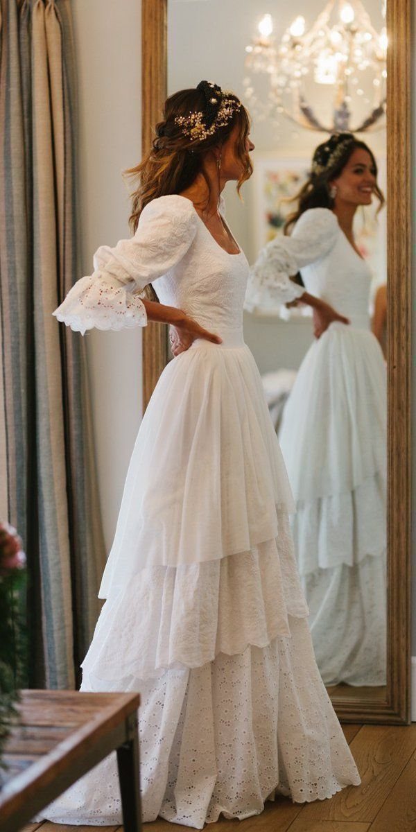 Woman in a white tiered wedding dress with lace sleeves posing in front of a mirror.