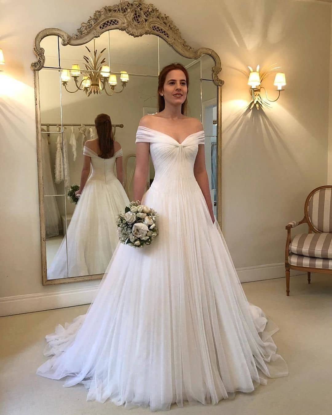 Woman in a white off-the-shoulder wedding gown holding a bouquet of flowers.