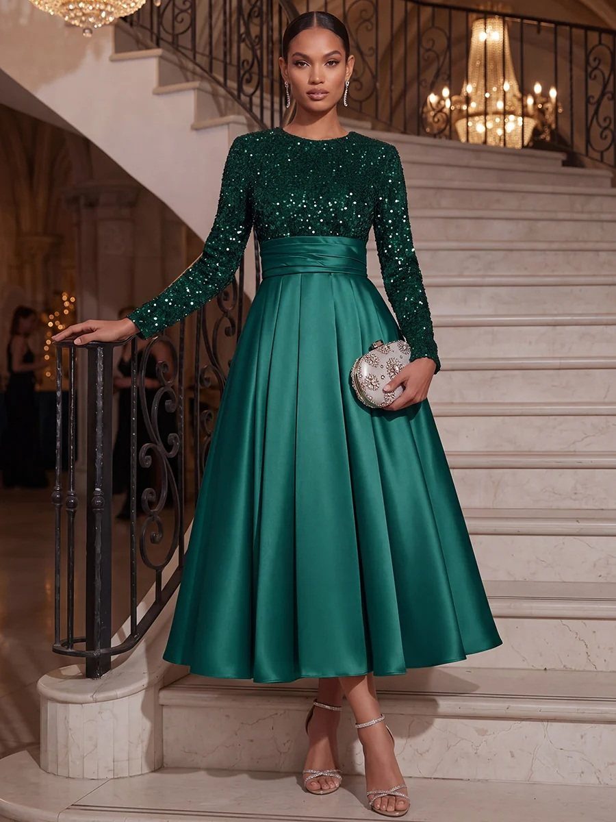 Woman in an emerald green sequined and satin midi cocktail dress posing on a staircase.