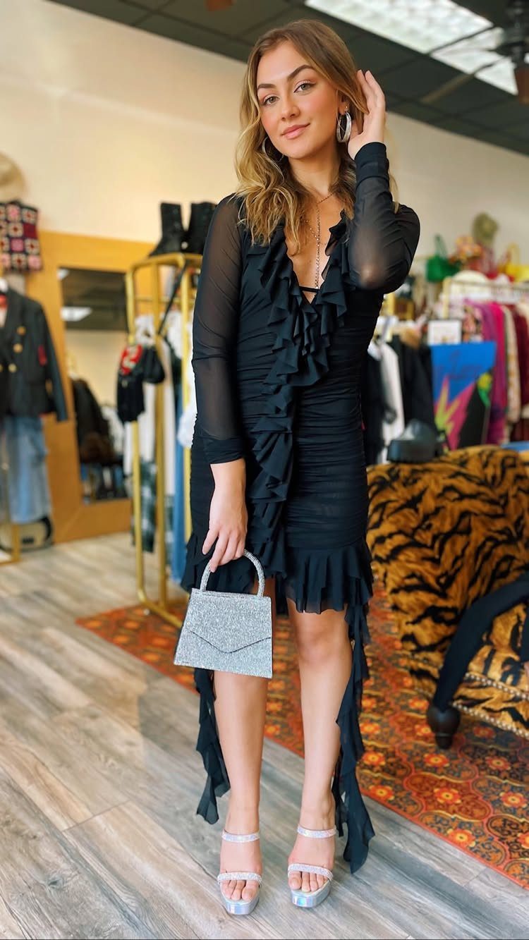 A woman wearing a black long-sleeved ruffled cocktail dress and silver accessories.
