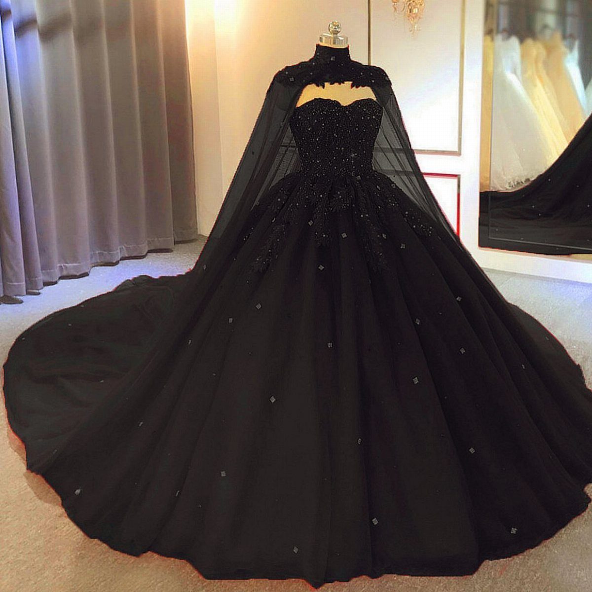 Black ballgown wedding dress with a beaded bodice and sheer capelet on a mannequin.