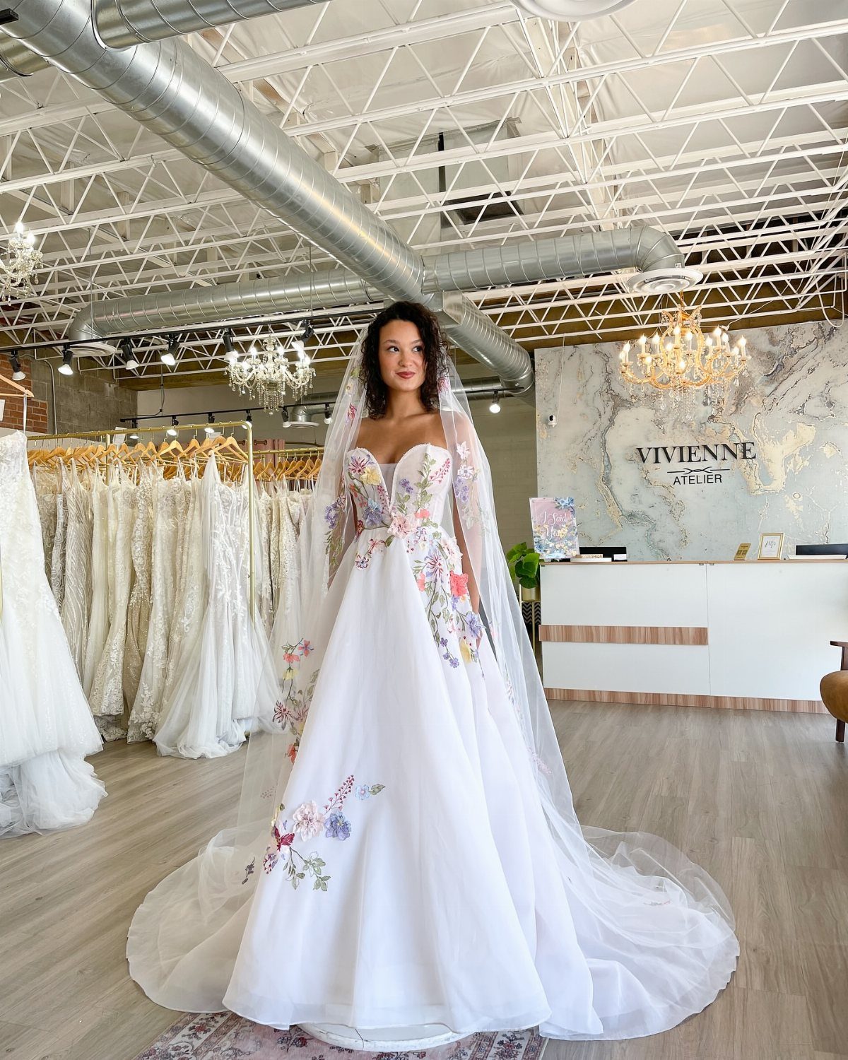 Woman wearing a white wedding dress decorated with colorful floral embroidery and a long veil.