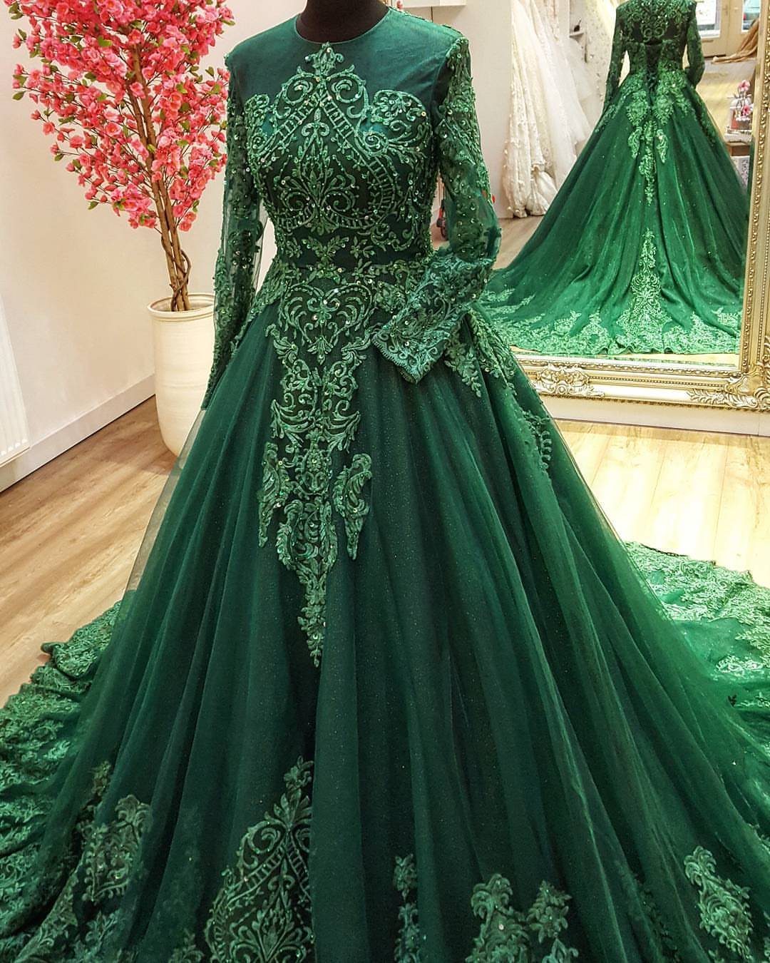 An emerald green lace wedding dress displayed on a mannequin in a bright boutique.