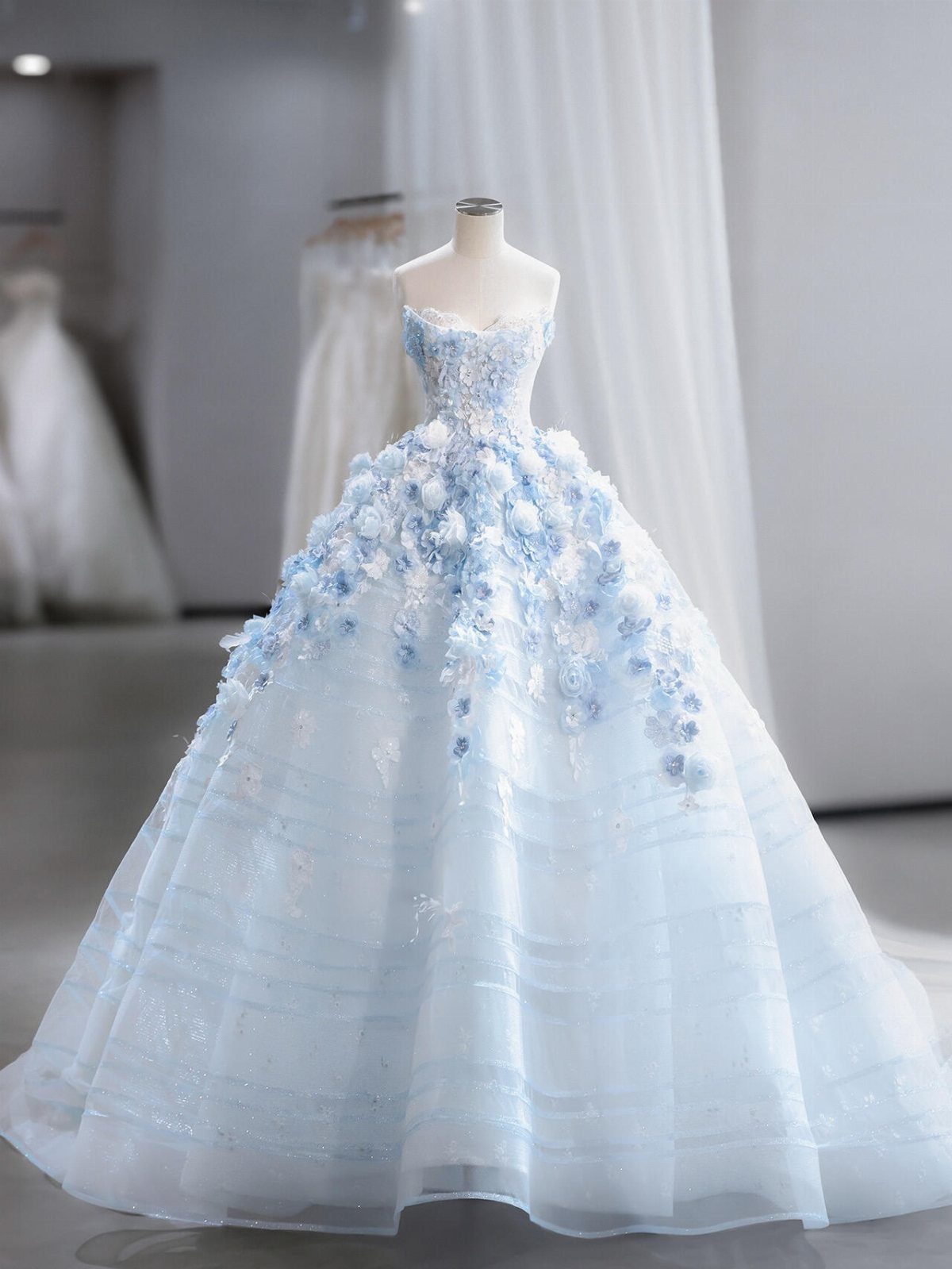 A light blue strapless wedding dress with large floral appliqués on a mannequin.