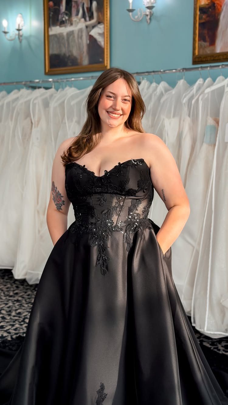 A smiling woman posing in a strapless black lace and satin wedding dress.