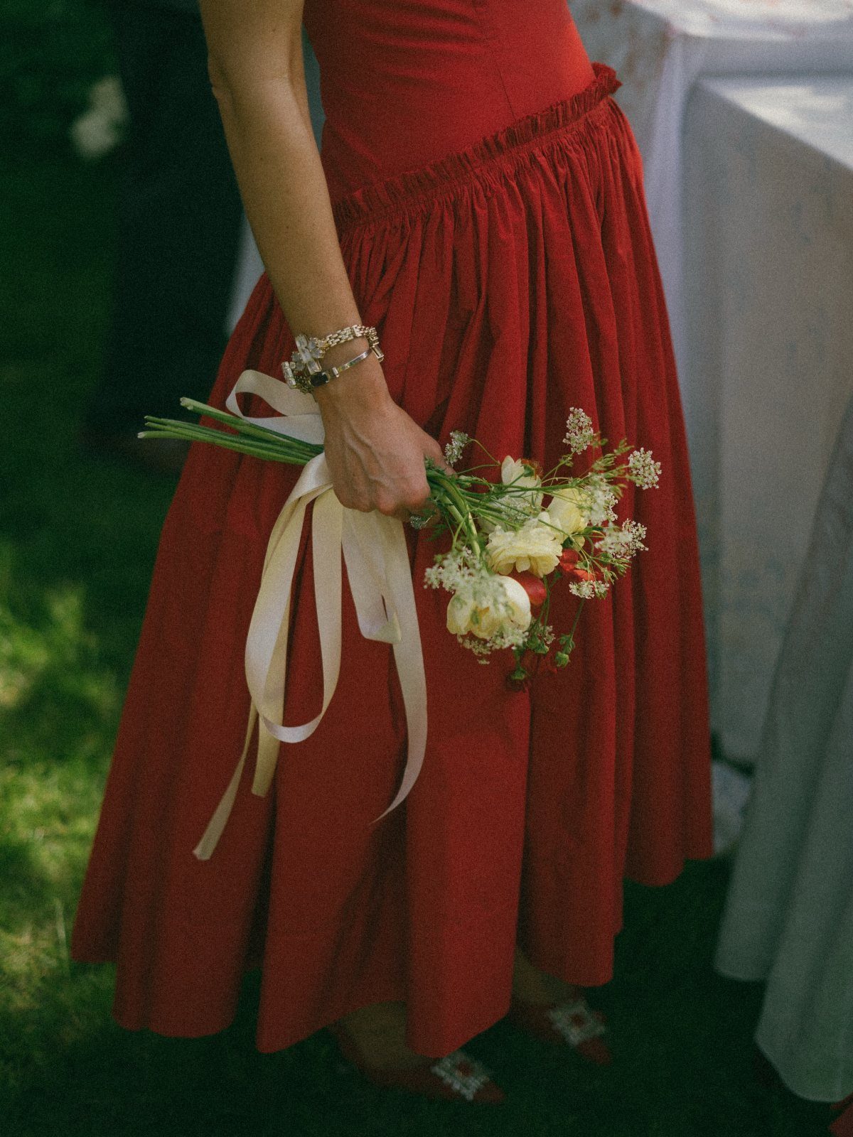 A person in a vibrant red dress holding a small bouquet of white flowers with long ribbons.