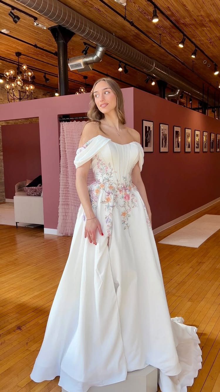 Woman in a white wedding dress with colorful floral embroidery standing in a boutique.