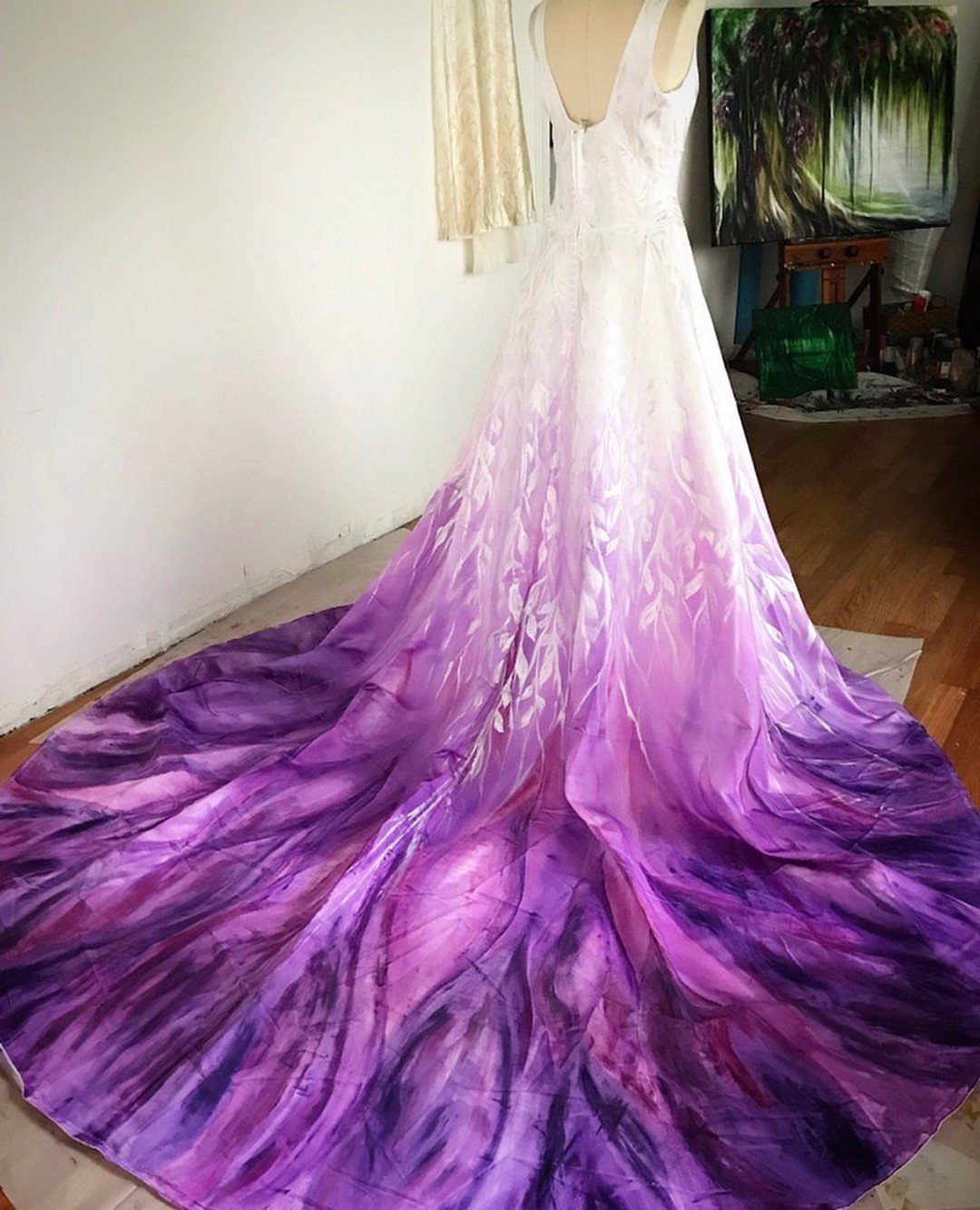 A white wedding dress featuring a dramatic purple ombre train with leaf patterns on a mannequin.