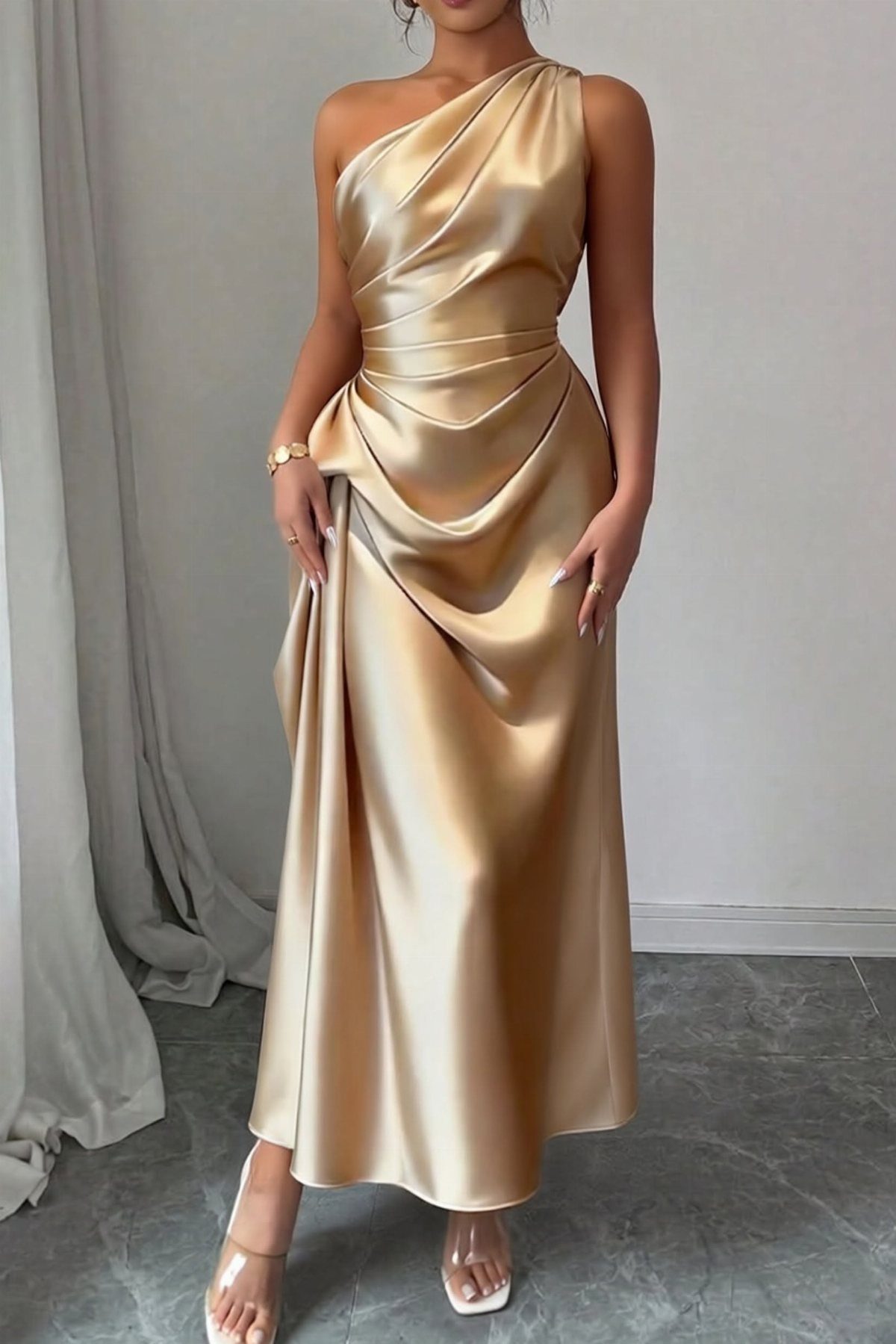 A woman posing in a gold one-shoulder floor-length satin gown with elegant draping.