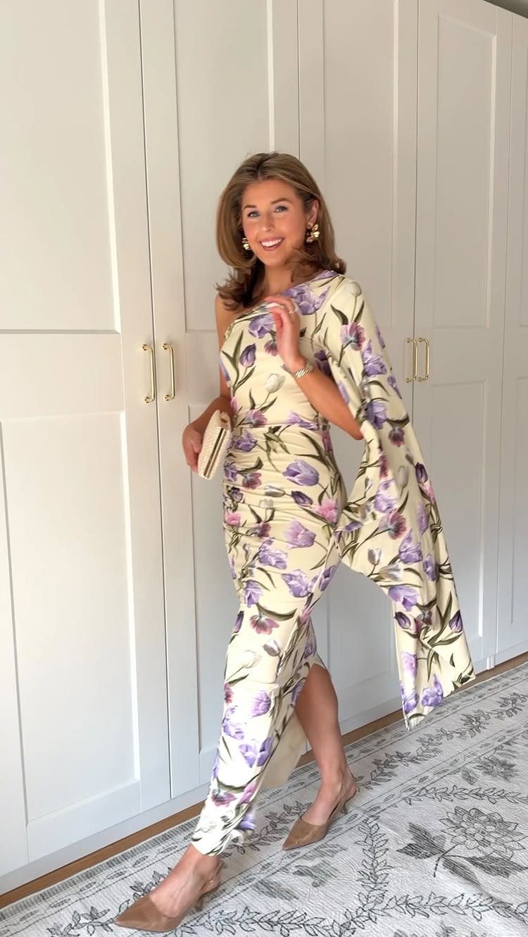 A woman posing in a cream floral maxi dress with a single long sleeve.