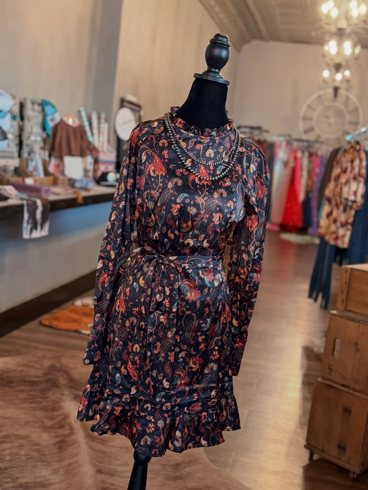 A floral patterned long-sleeved mini dress displayed on a black mannequin in a boutique.