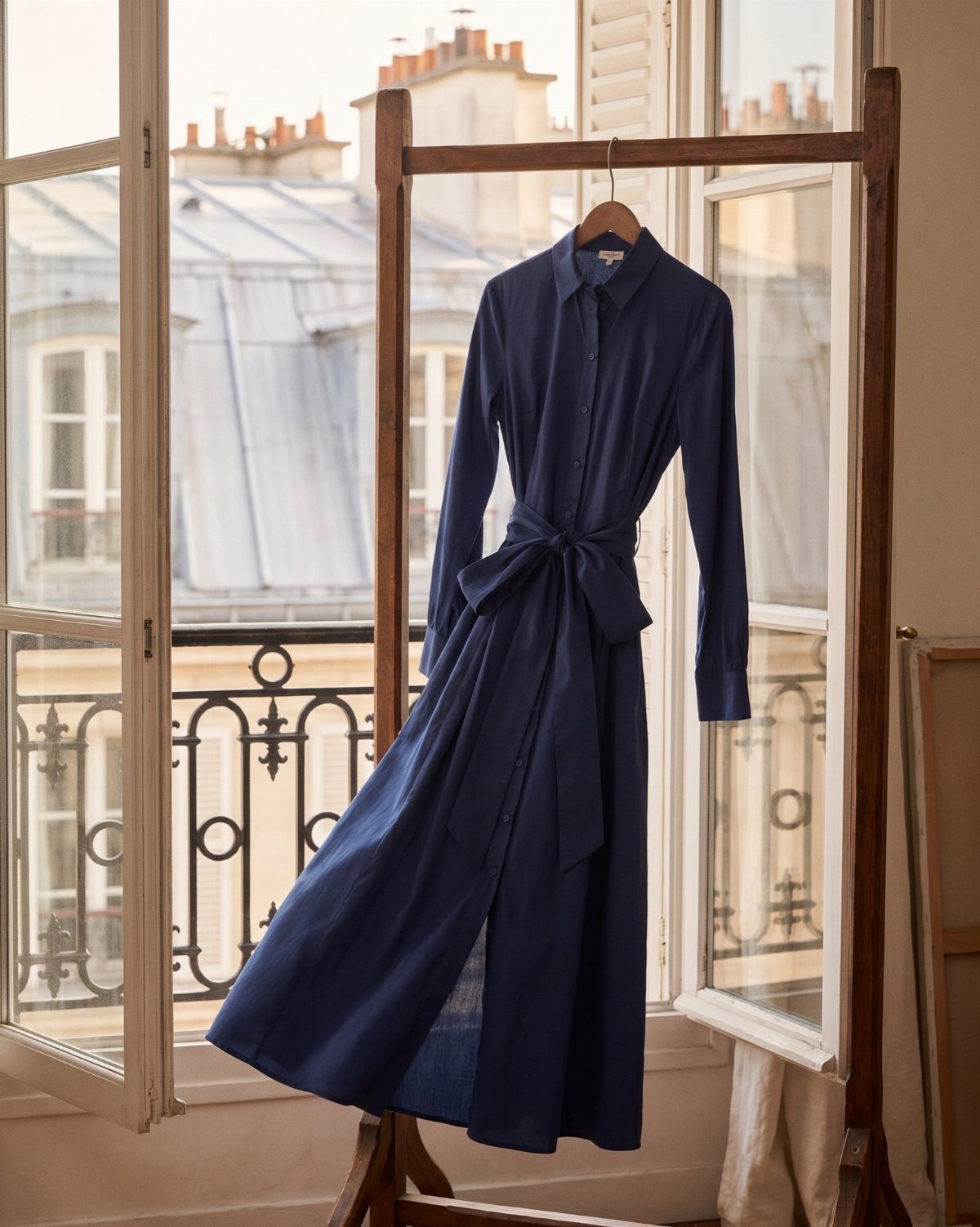 A navy blue long-sleeved midi dress hanging on a wooden easel by a window.