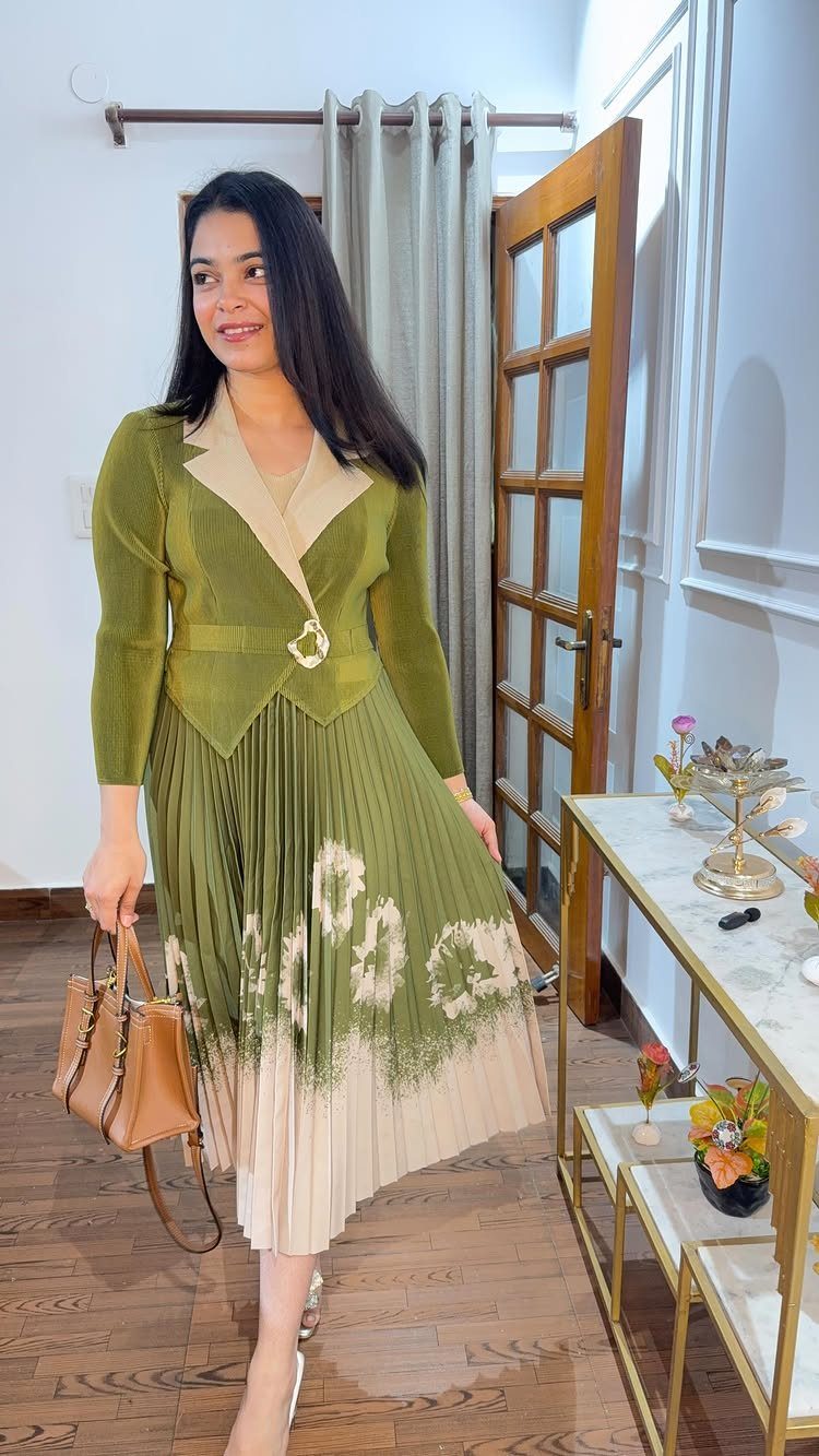 A woman posing in an olive green pleated midi dress with cream floral patterns.