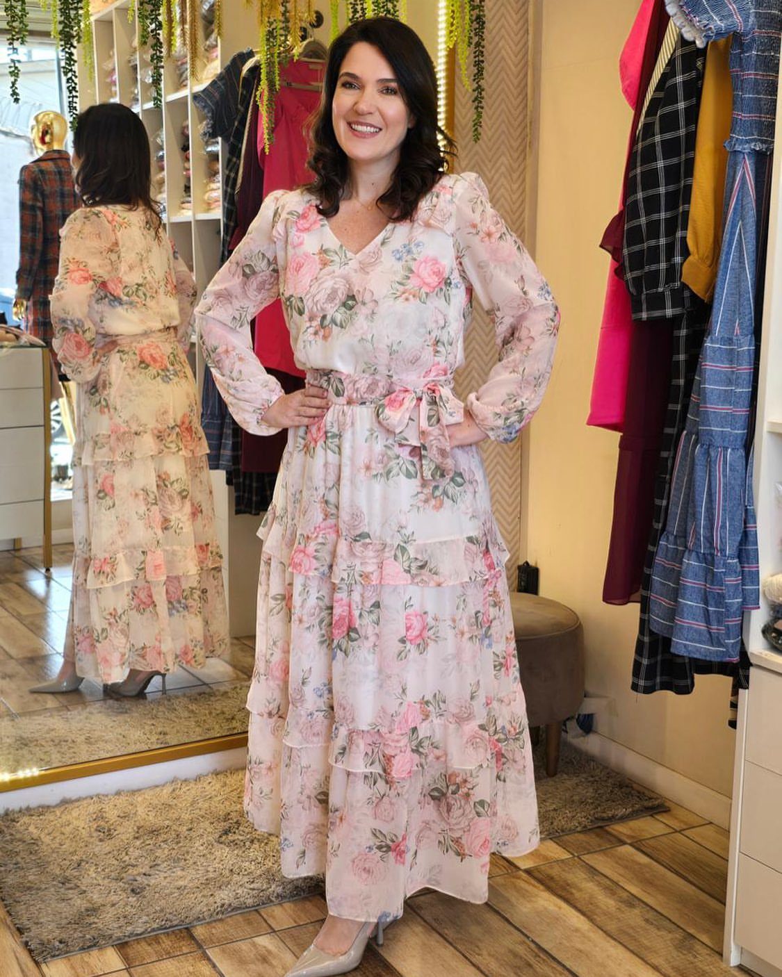 A woman smiling while wearing a long-sleeved pink floral midi dress with a tiered skirt.