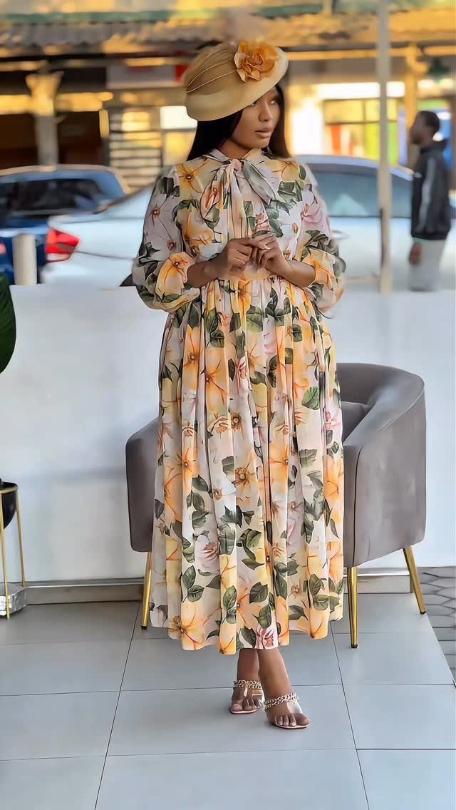 A woman posing in a long-sleeved floral midi dress and a matching decorative hat.