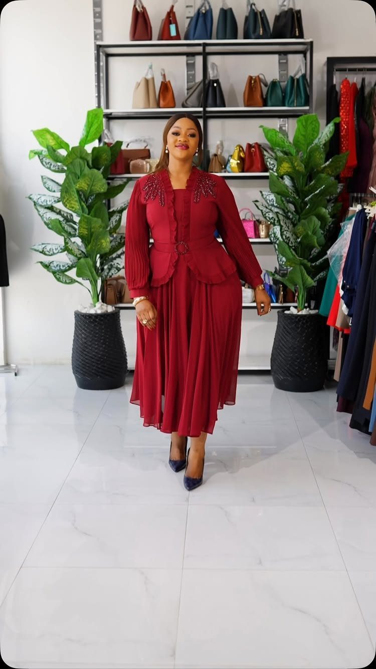 A woman posing in a red pleated skirt and matching beaded jacket outfit.