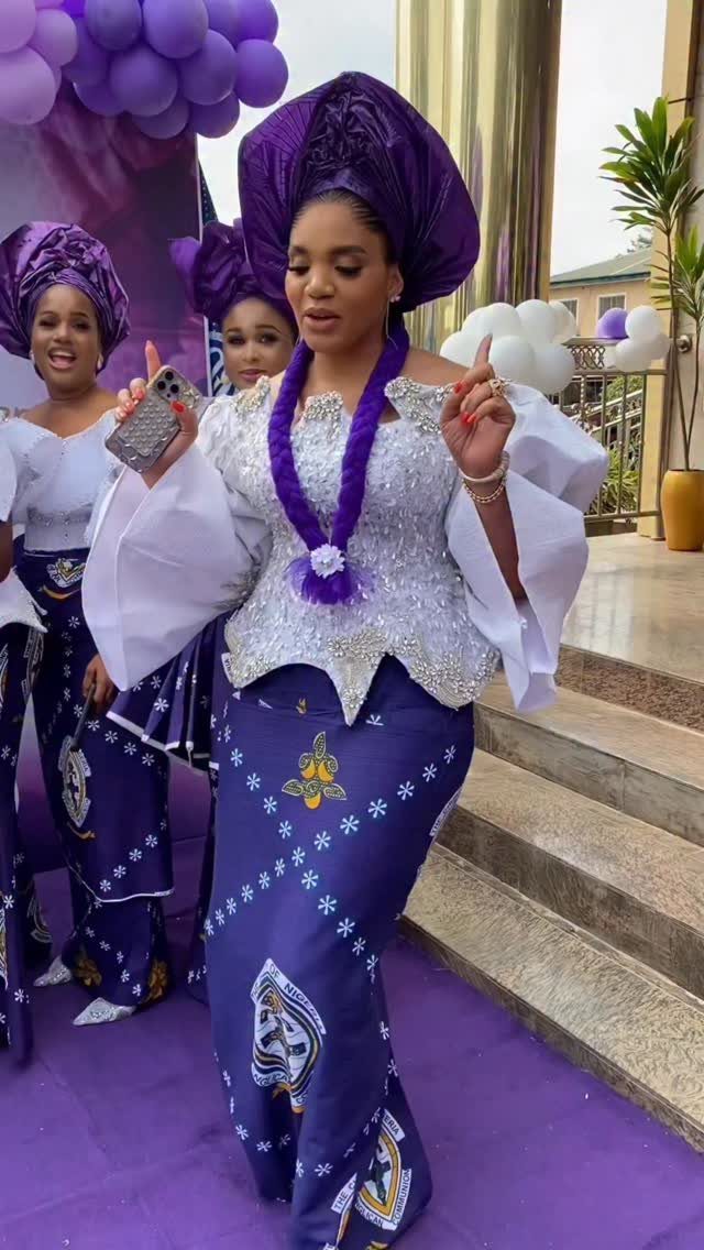 Women in matching purple and white traditional African attire walking on a purple carpet.